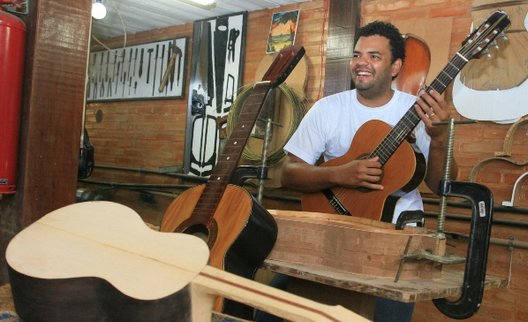 Foto de um professor da Escola Fundição de Artes e Ofícios, posando para foto com um dos violões confeccionados por ele