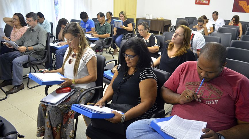 Foto dos profissionais da educação preenchendo documentos durante a posse do conselho