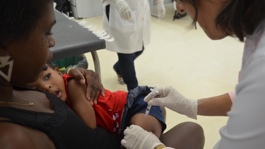 Foto de uma criança no colo da mãe sendo vacinada