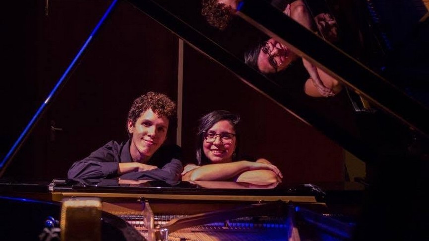 Foto dos artistas debruçados sobre o piando sorrindo