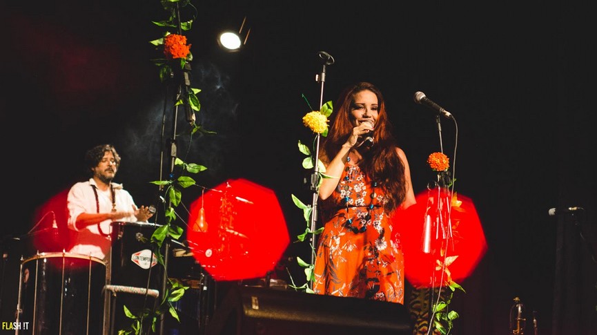 Foto da artista Renata Cabral no palco e ao fundo percussionista durante apresentação