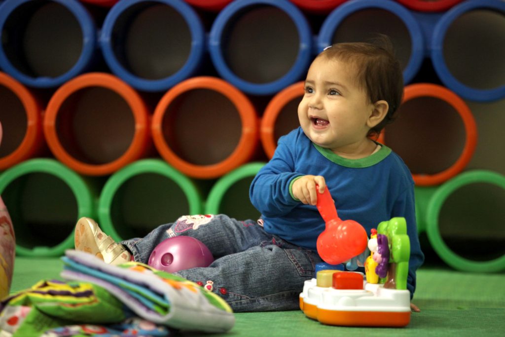 Criança com uniforme, sorridente, sentada e brincando