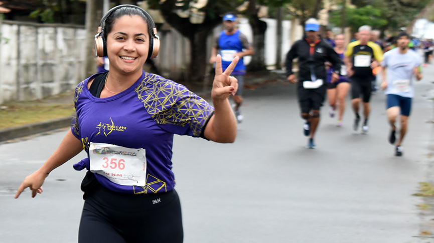 Na foto uma corredora faz sinal da paz e sorri enquanto corre em direção a camera