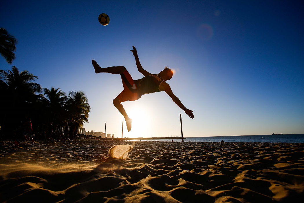 Na foto, um atleta aparece fazendo uma manobra de Futevôlei