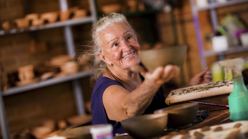 Uma senhora estendendo um pote feito de barro criado por ela como artesanato