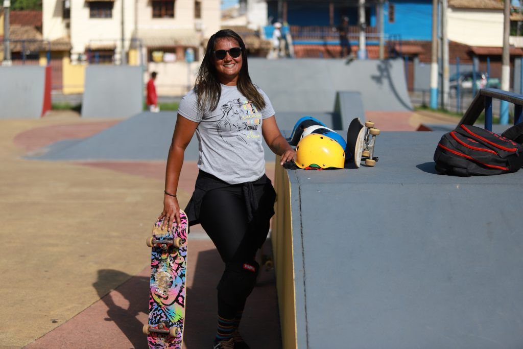 Atleta Juliana, sorrindo, segura skate com a mão