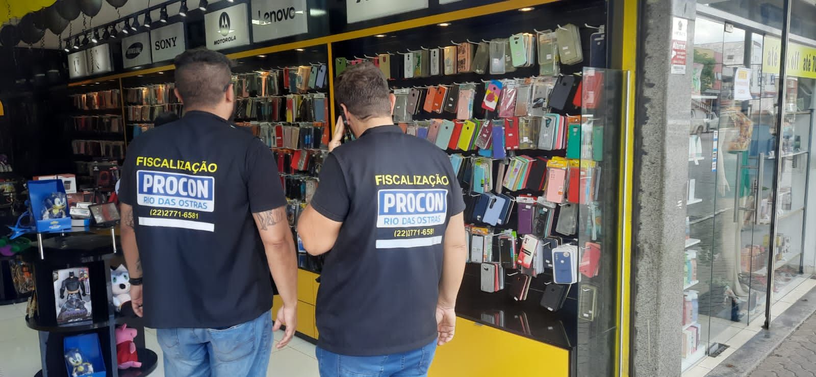 Fiscais do Procon de costas em loja de celulares e acessórios