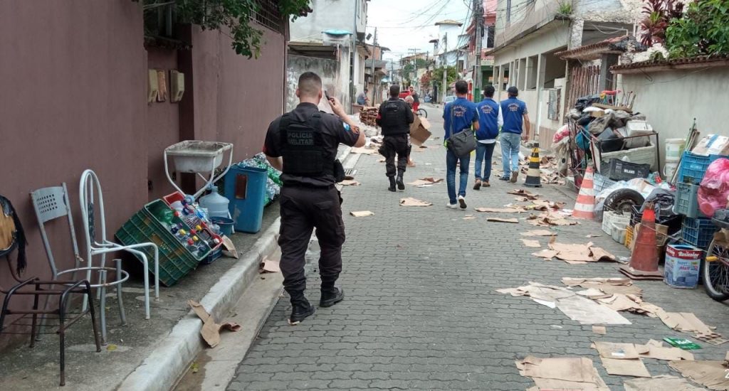 Policiais e fiscais caminham em rua com papelões no chão e entulhos nas calçadas