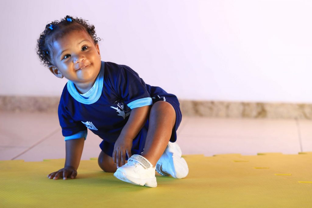 Bebê com uniforme sentada no chão e sorrindo