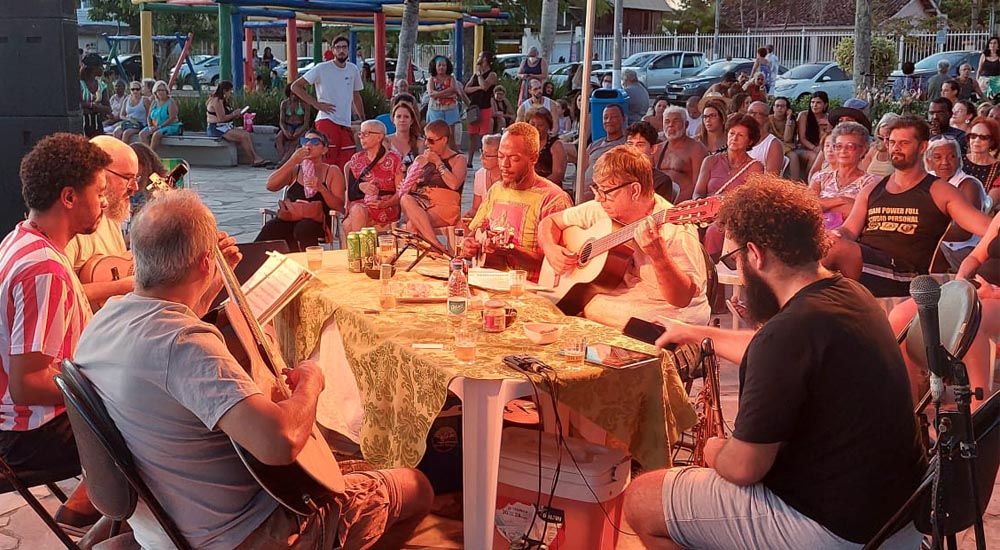 Músicos sentados tocam para plateia na praça