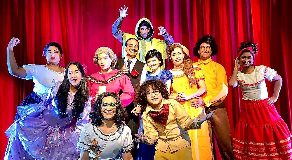 Artistas com roupas de personagens do filme Encanto no palco do teatro