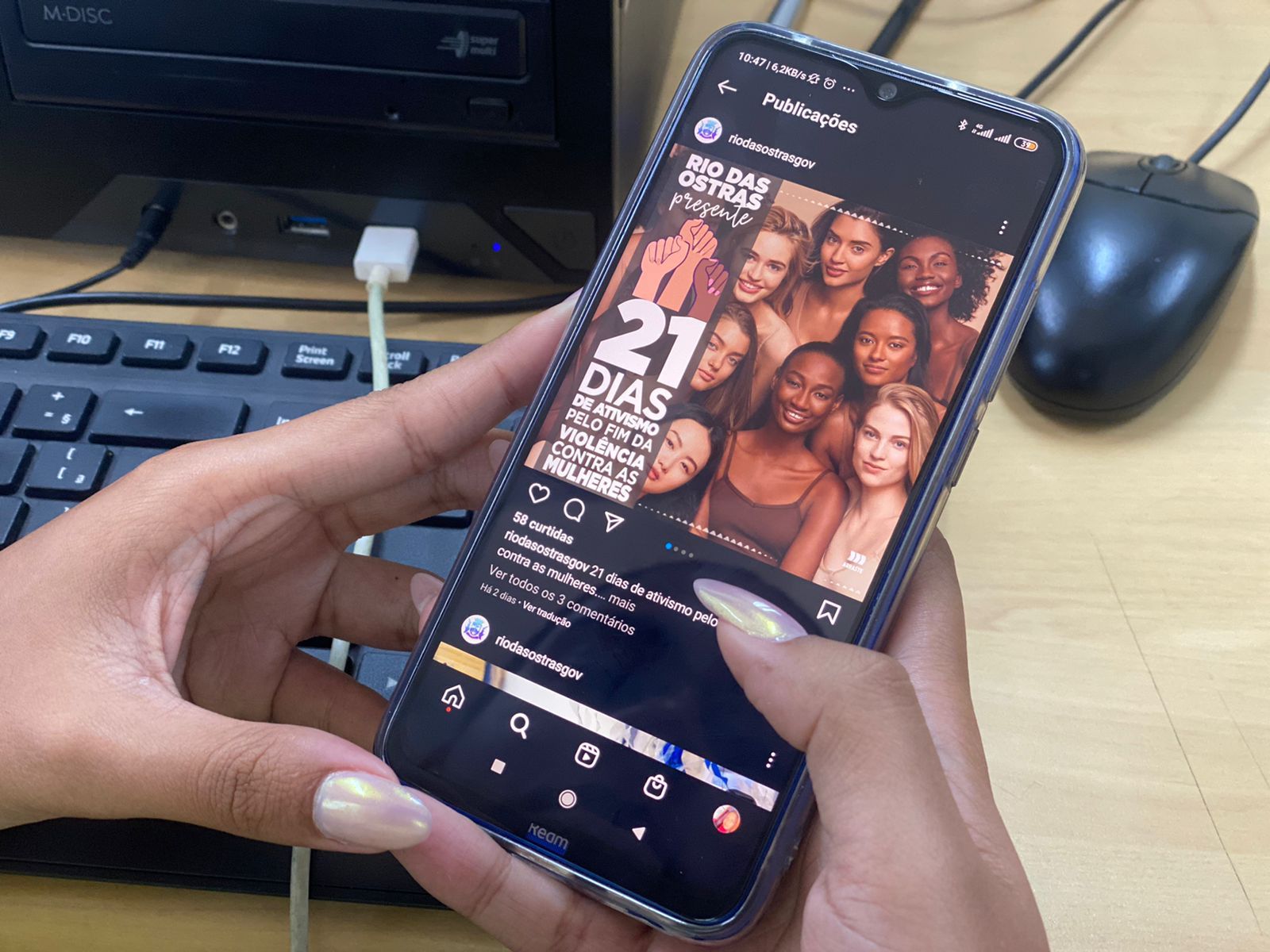Mão de mulher segurando um telefone celular. Na tela, uma postagem no instagram sobre a campanha.