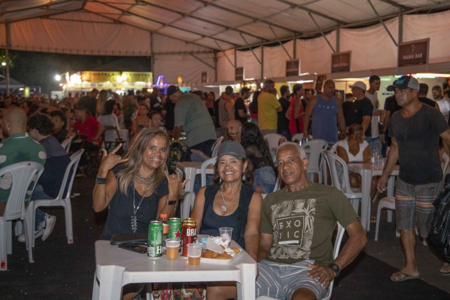 Na frente da foto, duas mulheres de meia idade sorridentes, acompanhadas de um homem também de meia idade, estão sentados na praça de alimentação