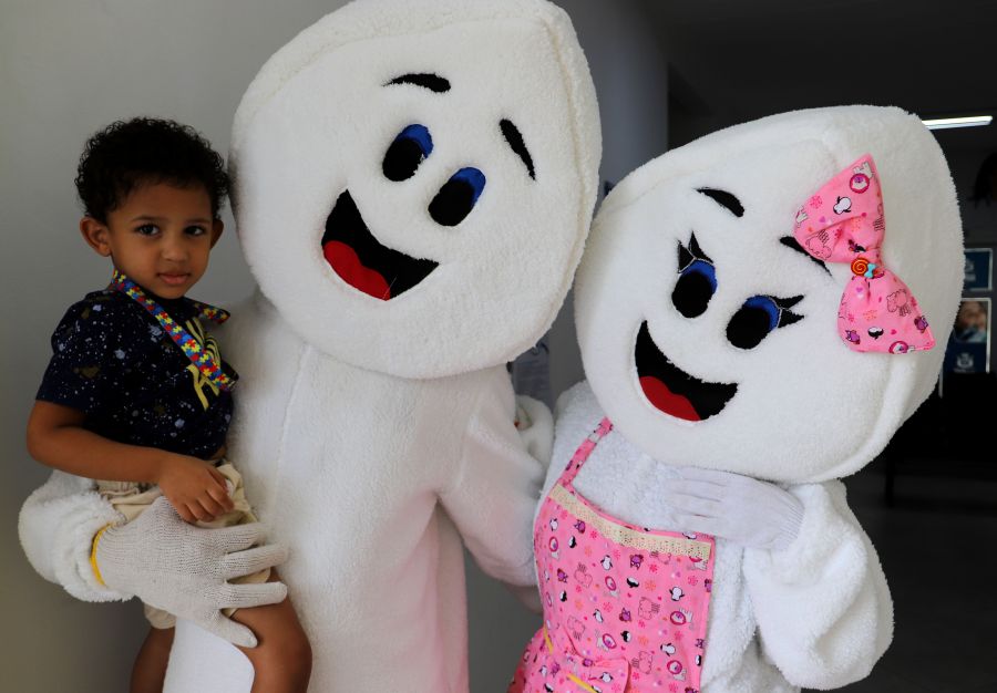 Dois mascotes da vacinação com uma criança no colo