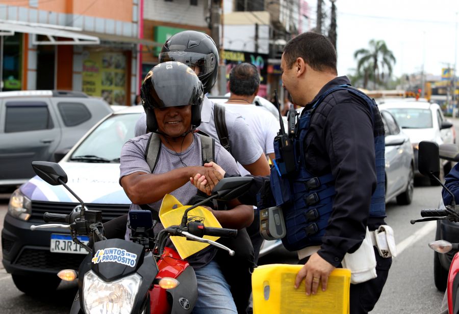 Agente cumprimenta motociclistas e entrega sacola de lixo veicular com material informativo