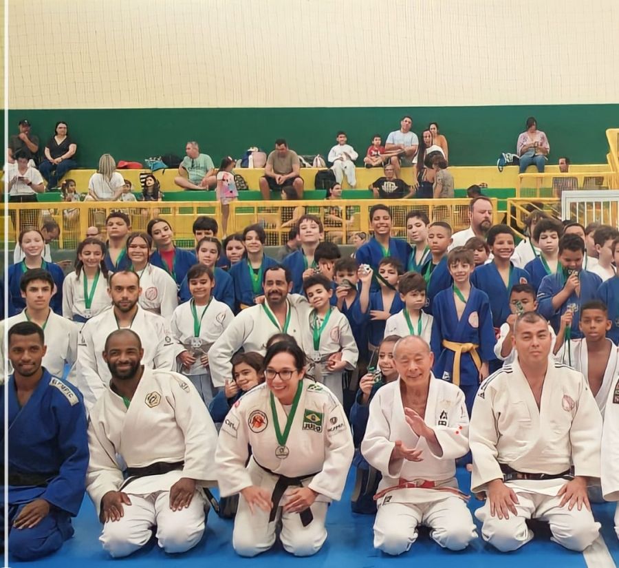 Na foto, em primeiro plano estão os professores de kimono com medalhas no pescoço. No fundo da foto, crianças de todas as idades estão com kimono de judô e medalhas recebidas durante o festival de judô.