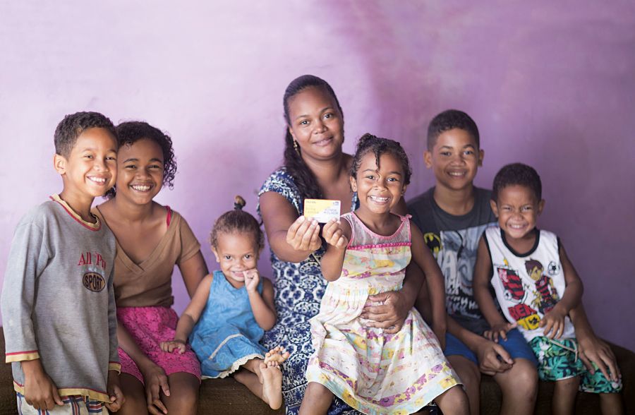 Uma mãe com seus seis filhos posando para foto com o cartão do Programa Bolsa família nas mãos