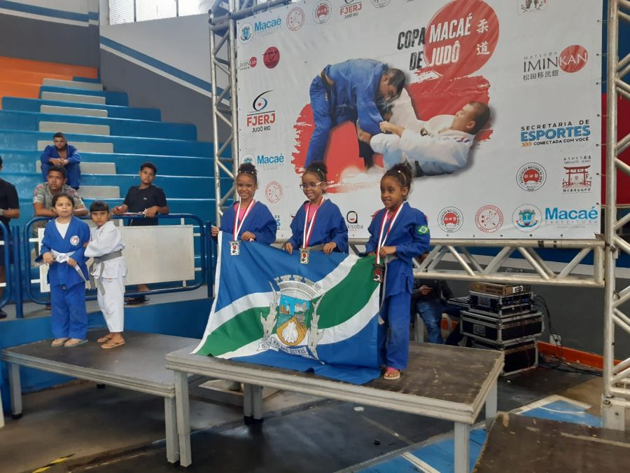 Na fotos, três atletas da categoria sub 9 seguram a bandeira do municipio e posam em um palanque com as medalhas no peito.