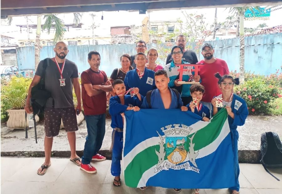 Na foto, toda a equipe de Judô de Rio das Ostras posa para foto segurando a bandeira de Rio das Ostras.