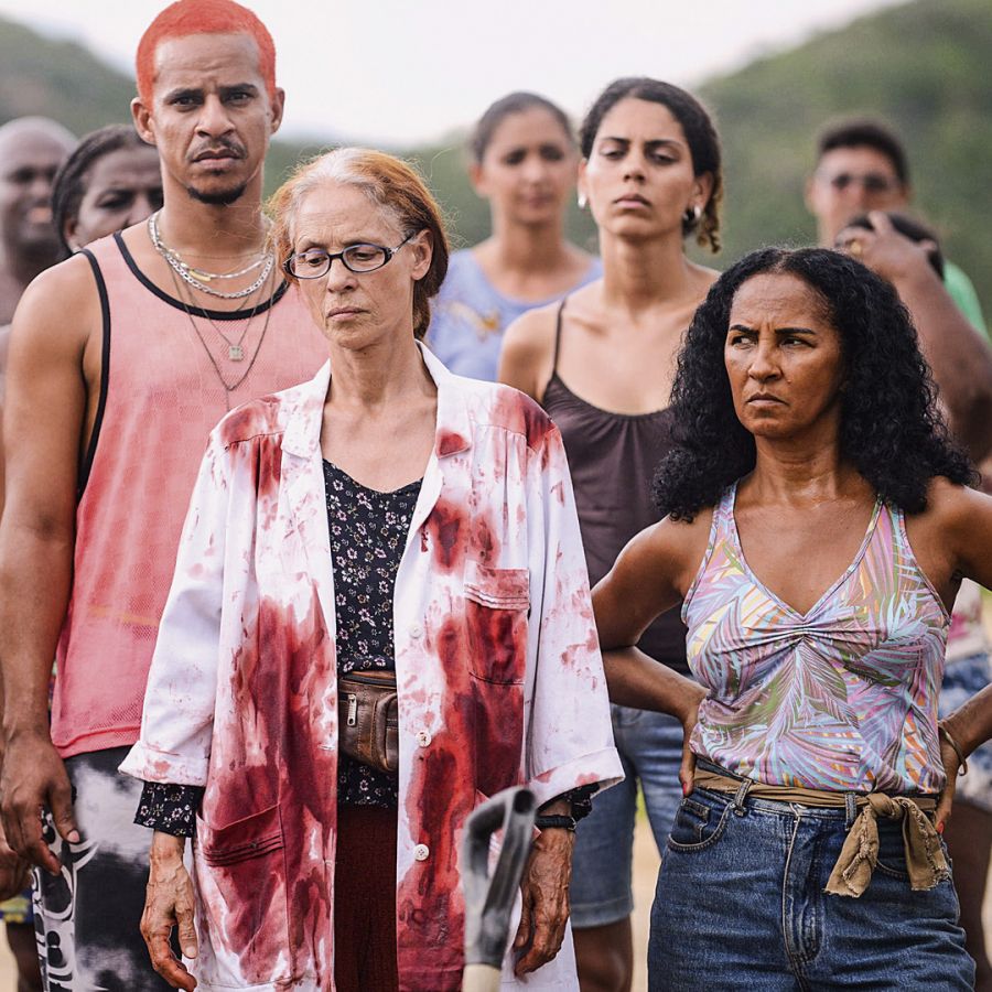 Cena do filme com moradores reunidos e, à frente, a personagem de Sônia Braga com jaleco sujo de sangue
