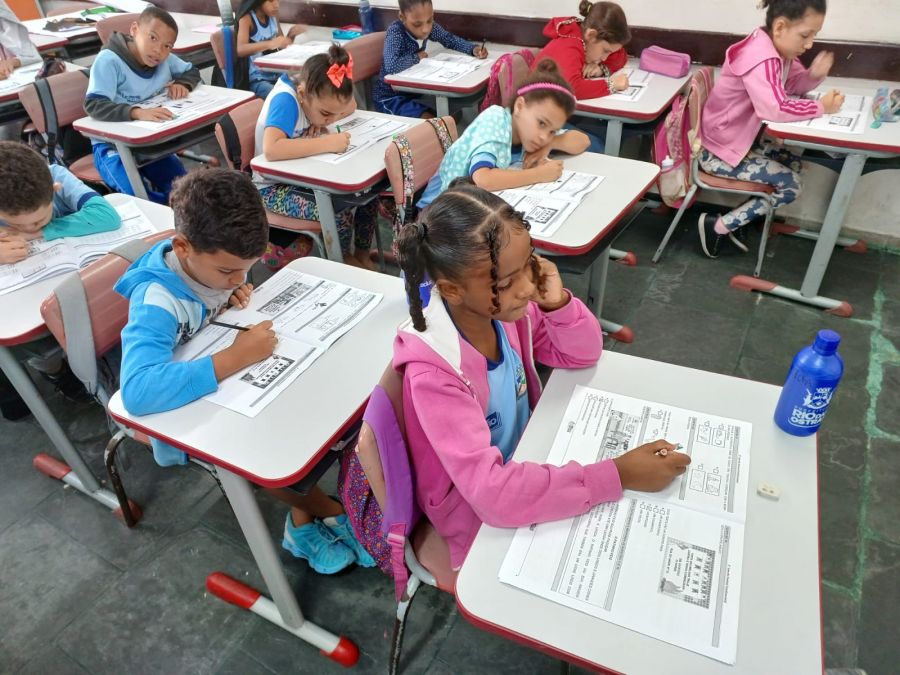 Alunos enfileirados em sala de aula com caderno de prova