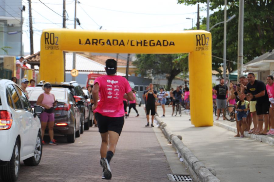 Na foto, um atleta de camisa rosa segue em direção a uma linha de chegada.