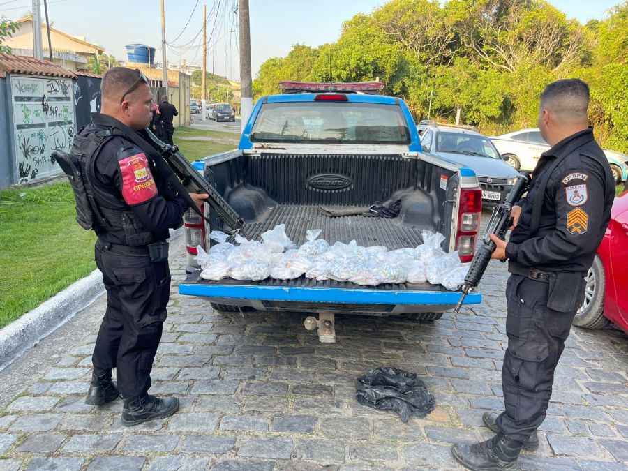viatura parada com dois policiais a frente com a caçamba aberta com sacolas de drogas
