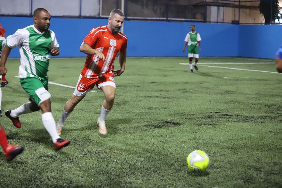 Na foto dois atletas disputam uma bola em um jogo de futebol em grama sintética