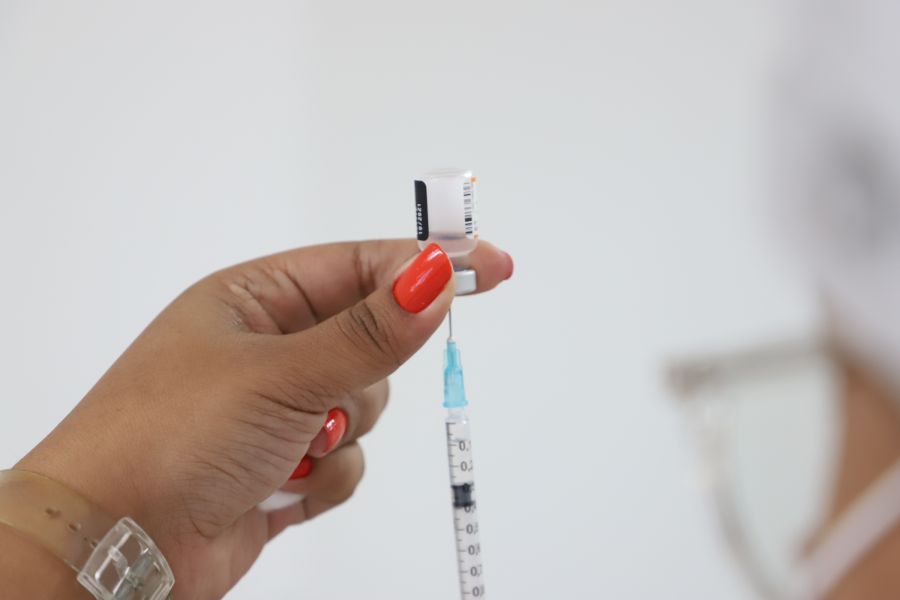 Uma mão segura a vacina contra a covid e a puxa com a seringa o líquido
