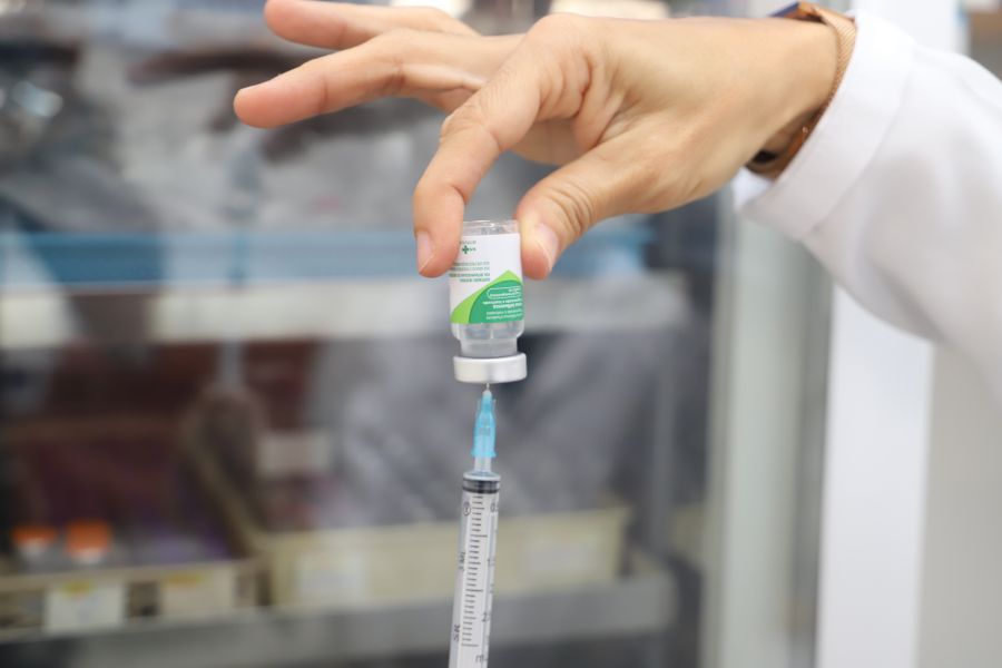 Frasco de vacina com a seringa e uma mão puxando o líquido