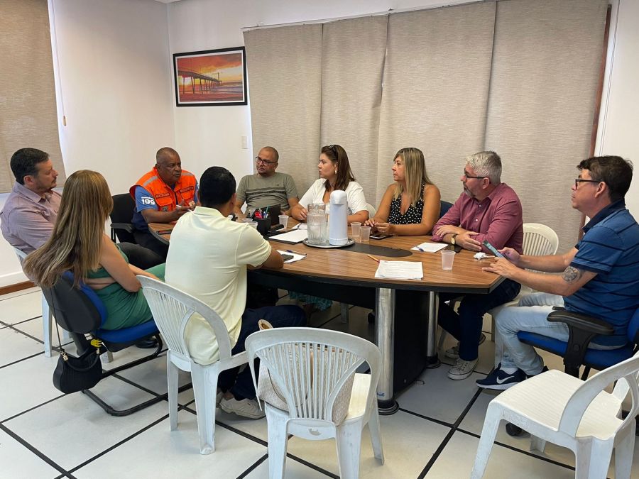 Autoridades de Rio das Ostras aparecem sentadas em volta de uma mesa prestando atenção ao coordenador da defesa civil.