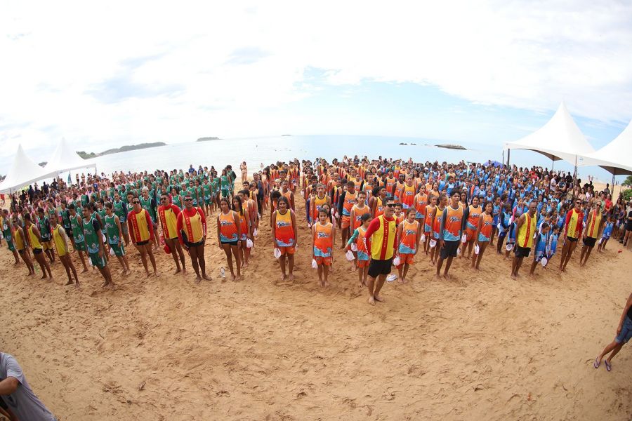 Na foto, crianças e adolesncentes estão perfilados e uniformizados na praia esperando o inicio do projeto.
