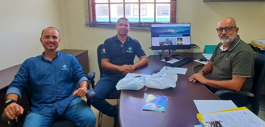 Três homens sentados ao redor da mesa sorriem para a foto