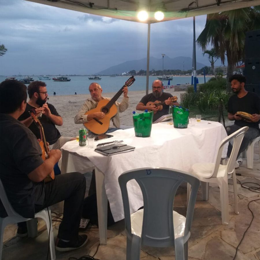 Ao pôr do sol, debaixo de uma tenda, cinco músicos tocam seus instrumentos
