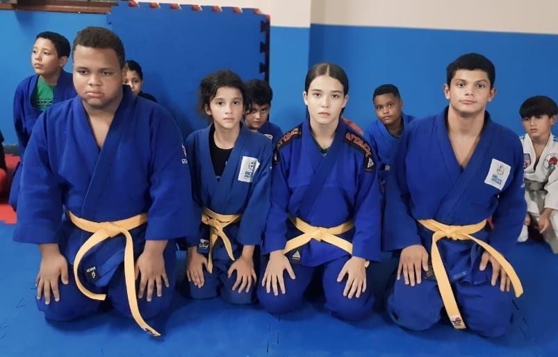 Na foto quatro judocas aparecem ajoelhados em um tatamos, todos utilizando o kimono azul fornecido pela prefeitura e todos com faixas marrons de suas categorias.